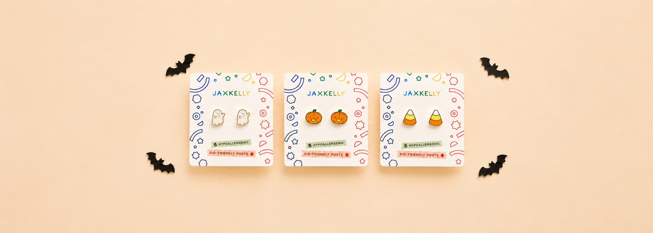 Three JaxKelly earring sets on cards: white ghosts, orange pumpkins, and candy corn, with small black bat decorations, all on a pale peach background.