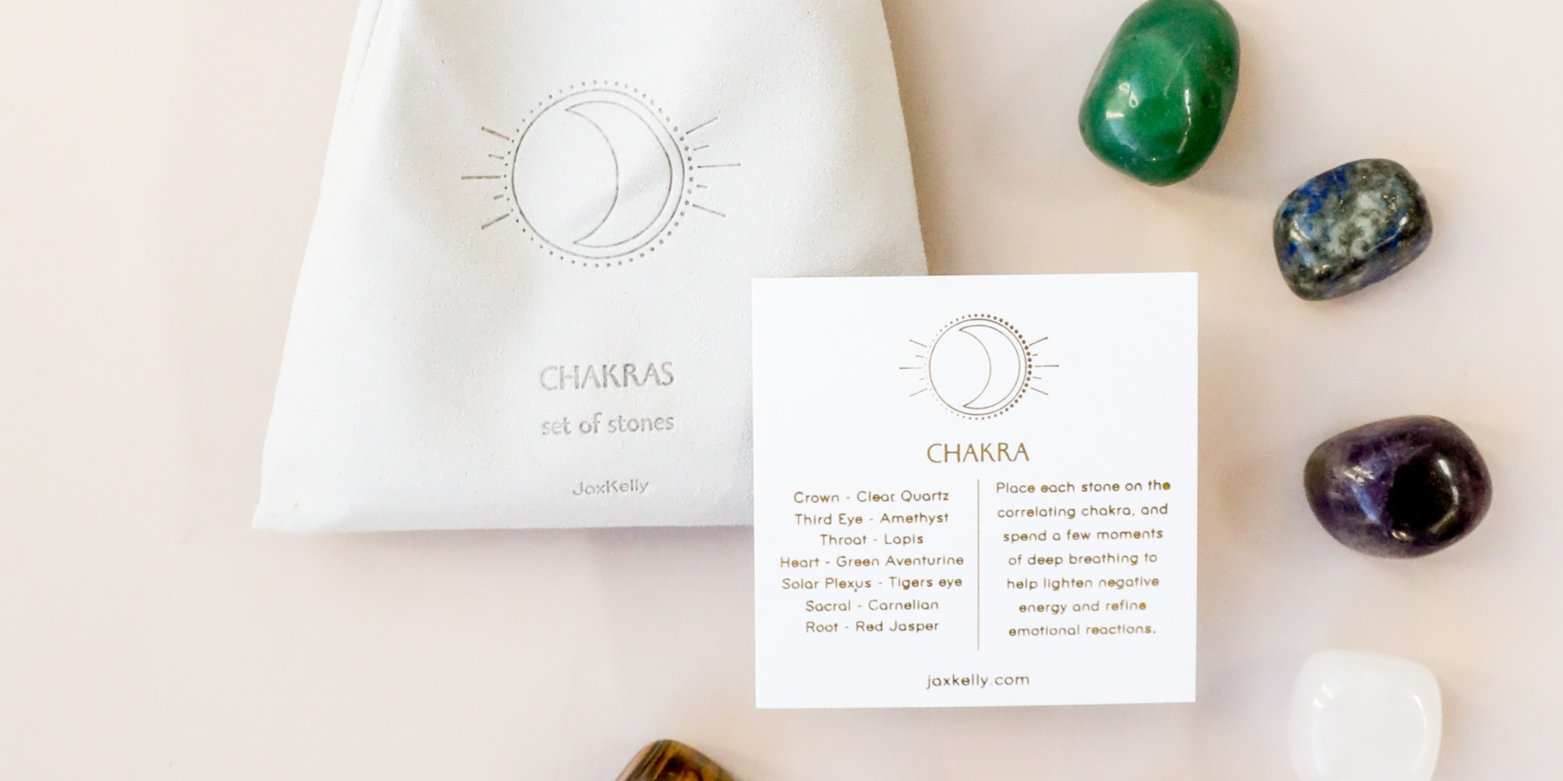 A white pouch labeled Chakras set of stones sits next to a card with chakra information, surrounded by colorful healing stones on a light surface.