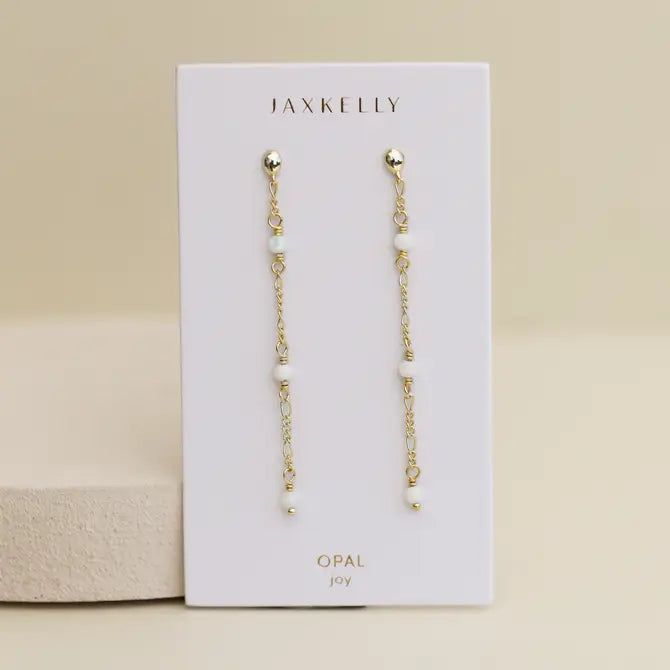 The JaxKelly Gemstone Chain Drop - White Opal earrings feature white opal beads and 18k gold plating, displayed on a branded OPAL joy card against a neutral background.