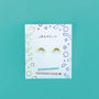 Rainbow Enamel Flat Back Kids Earrings, hypoallergenic and kid-friendly, are displayed on a white card with colorful geometric doodles labeled JaxKelly—perfect for sensitive ears—set against a teal background.
