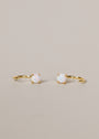 The White Opal Huggie features delicate gold hoops, each adorned with a small lab-grown opal in a four-prong setting, showcased on a neutral beige background.