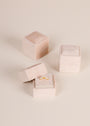 Three JaxKelly Square Velvet Jewelry Boxes in light pink are displayed, with one open to show a gold sunburst ring inside as a compact organizer, while the other two remain closed on a light surface.