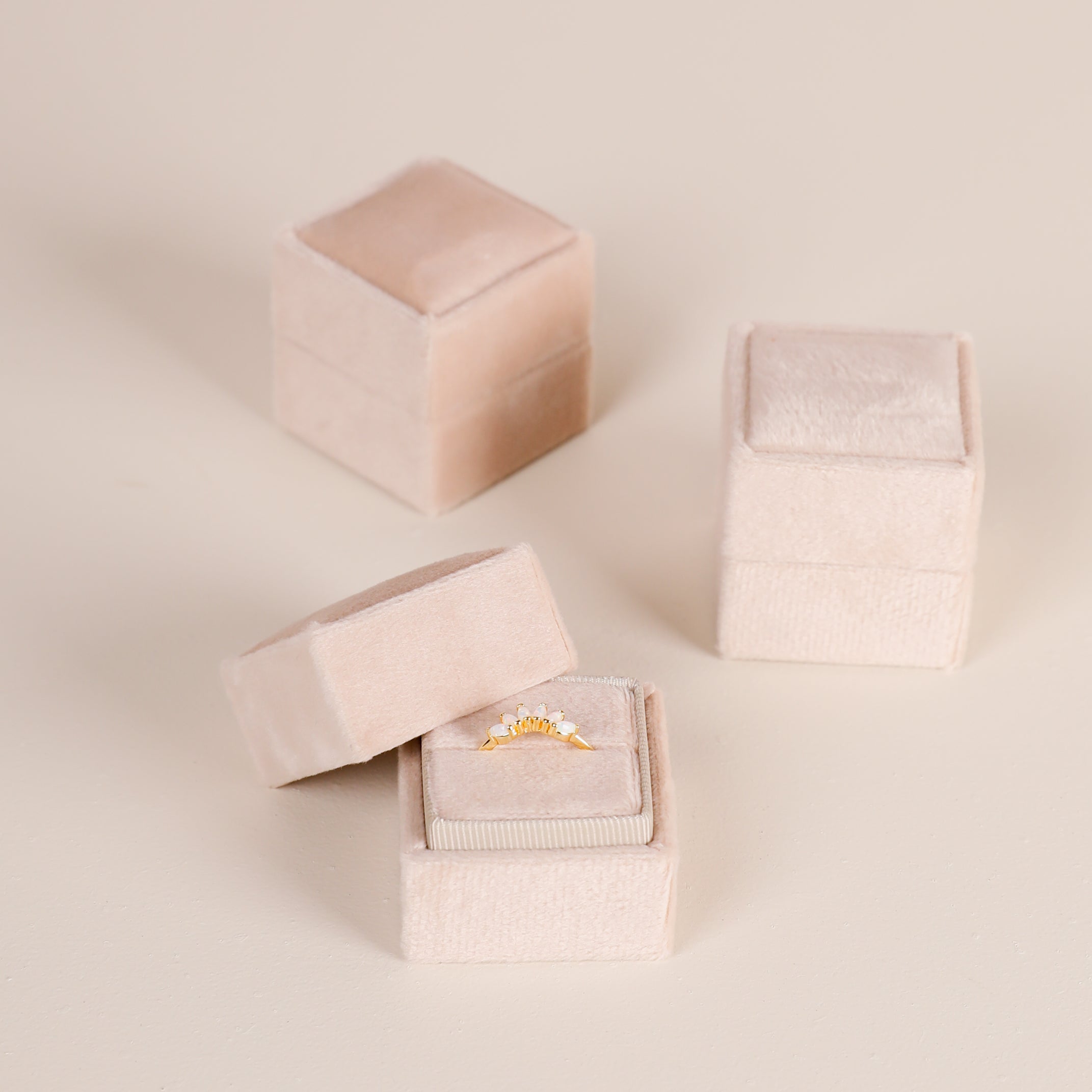 Three JaxKelly Square Velvet Jewelry Boxes in light pink are displayed, with one open to show a gold sunburst ring inside as a compact organizer, while the other two remain closed on a light surface.