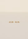 The Double Champagne Hoop Earrings feature a small, double offset design with 18K gold plating and two rows of pave stones, shown against a plain light beige background.