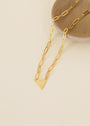 The Gold Heart Pendant Link Chain Necklace - 18k Gold Plated features elongated links and a small heart charm, displayed on a round beige ceramic dish against a light cream background.