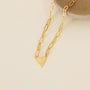 The Gold Heart Pendant Link Chain Necklace - 18k Gold Plated features elongated links and a small heart charm, displayed on a round beige ceramic dish against a light cream background.