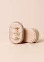 The Small Oval Velvet Jewelry Box holds three delicate gold rings with geometric designs, displayed against a soft beige background.