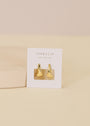 A pair of Small Ripple Gold Hoop earrings with sterling silver posts displayed on a white JaxKelly card reading "Wear Good Vibes," set against a soft beige background.