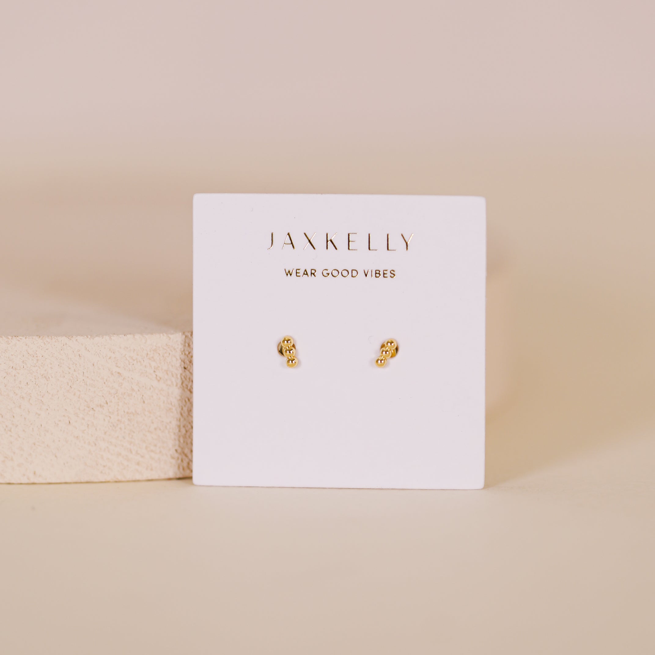 The Petite 3 Ball Gold Earrings feature a minimalist trio design with 18K gold plating, displayed on a JaxKelly card reading "Wear Good Vibes" against a neutral background.