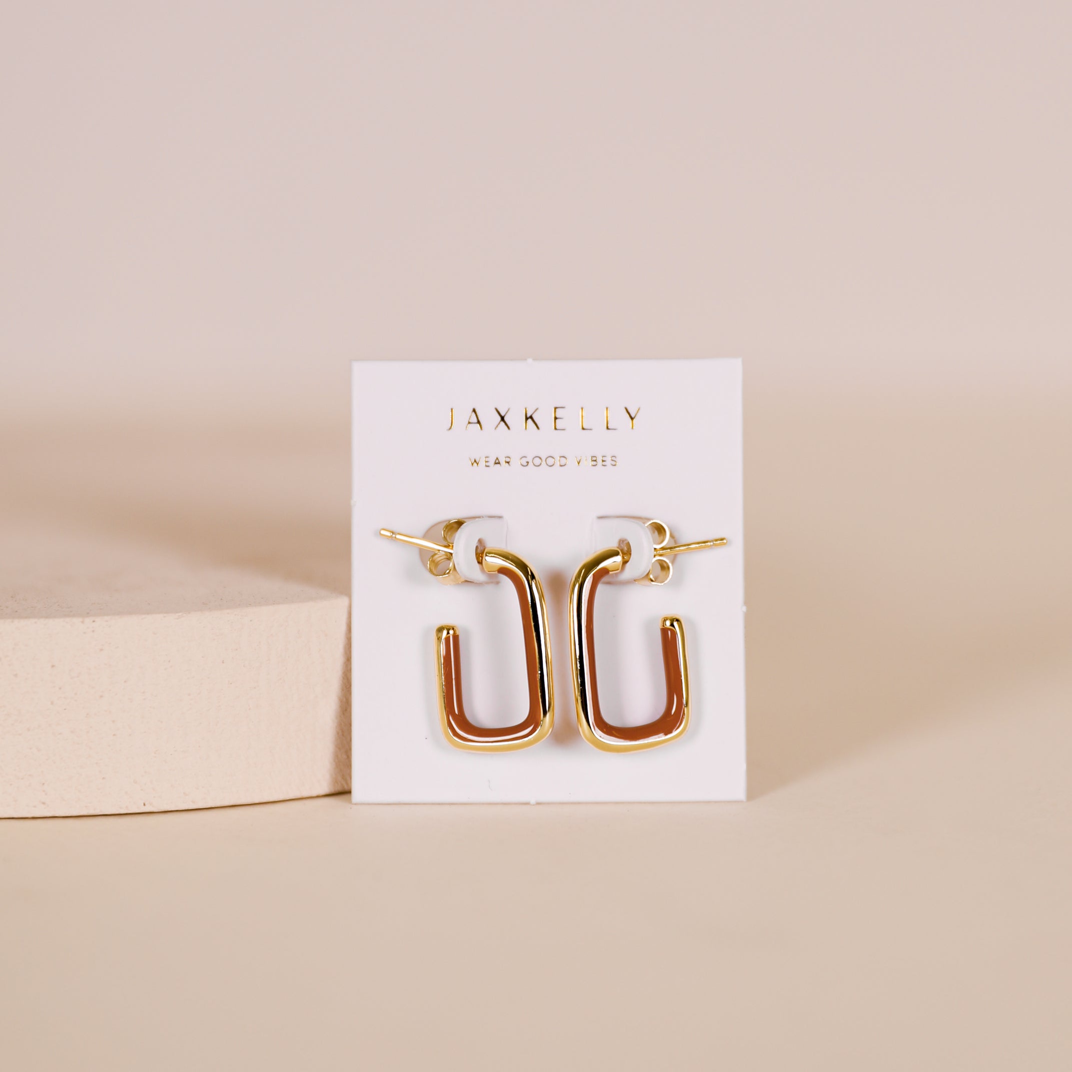 Brown Enamel Large Rectangle Gold Hoop Earrings displayed on a JaxKelly-branded white card against a beige background. These 18k gold-plated hoops feature brown enamel for a modern, stylish touch to any outfit.
