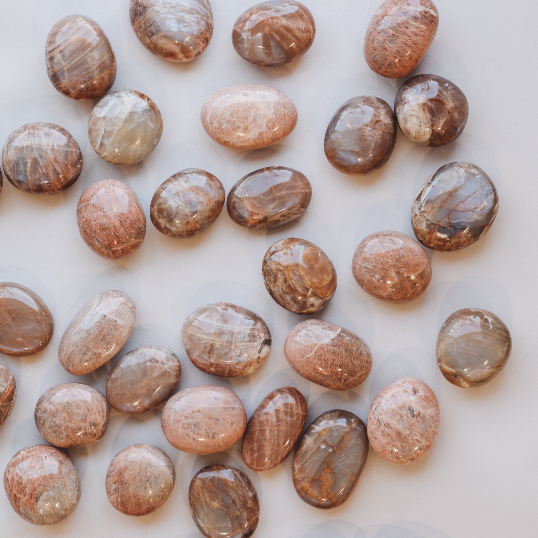 A set of smooth, oval Moonstone Palm Stones for luck, featuring genuine brown and tan crystals with natural patterns, scattered on a light surface and reflecting light.