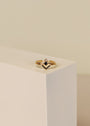 The Black Infinity Ring, featuring black cubic zirconia and a clear stone, is displayed on the corner of a white geometric block against a neutral background.