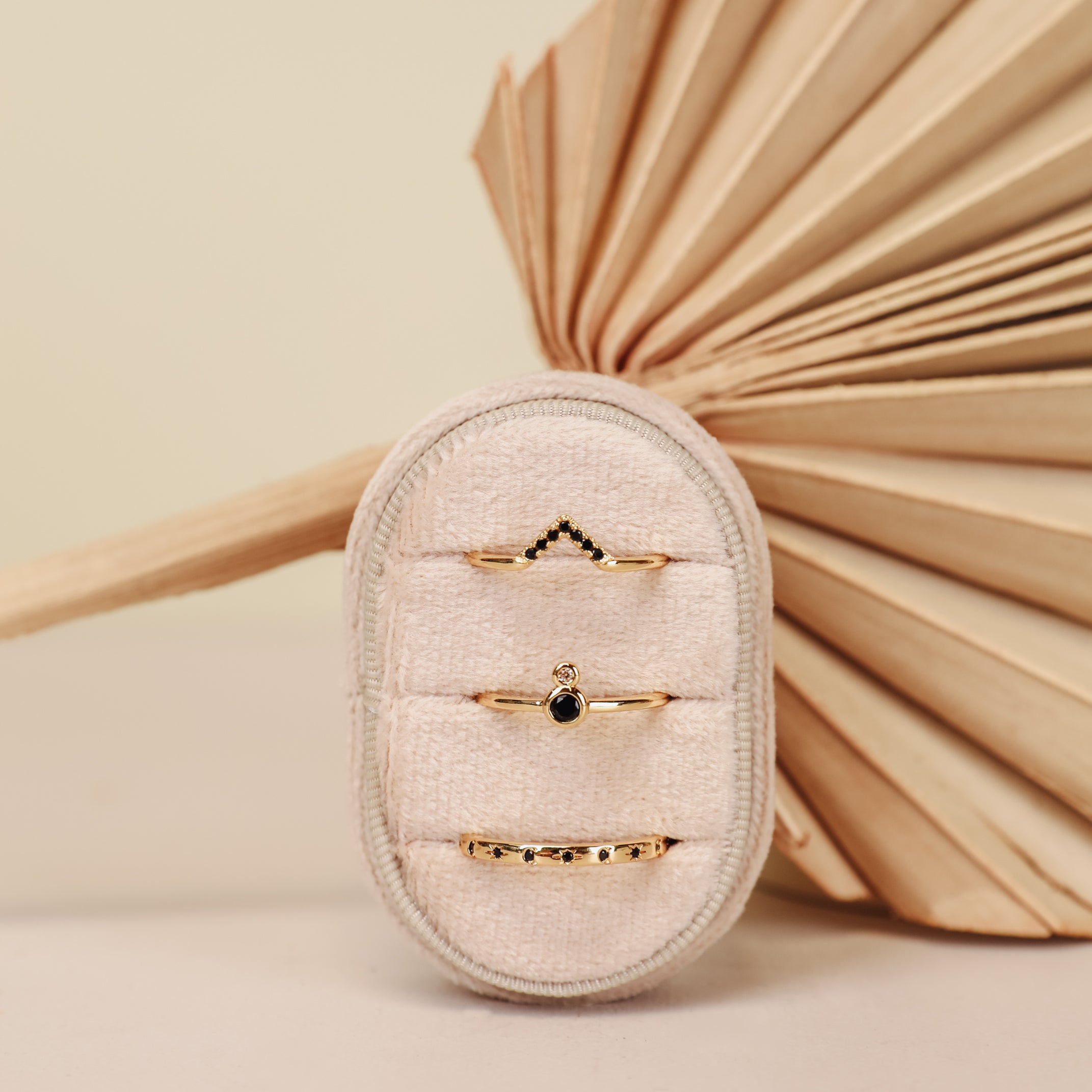 The Black Infinity Ring, an elegant 18k gold-plated piece, is showcased vertically on a soft beige ring holder with a folded dried palm leaf and a neutral background for decoration.