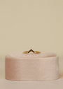 The Black Lambda Ring, a gold plated piece with a chevron design and small dark stones, is shown upright on a soft, round, light pink velvet stand—ideal for stacking against a neutral backdrop.