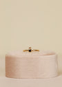 The Black Infinity Ring, an 18k gold plated piece with a small black cubic zirconia and a tiny clear stone above it, is shown upright on a soft pale pink oval ring holder against a neutral background.