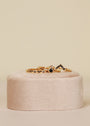 The Black Infinity Ring, a delicate 18k gold plated piece with small black cubic zirconia stones, is showcased on a soft round beige velvet stand against a light neutral background.