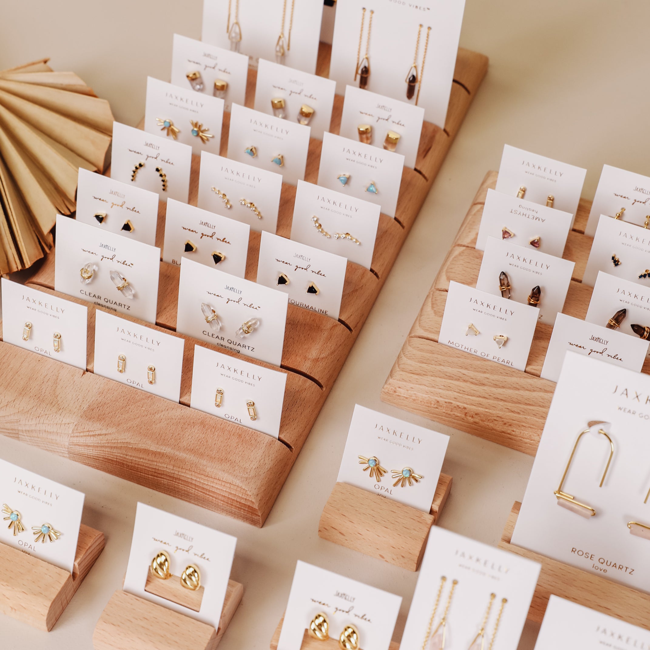 Gold earrings and necklaces, including the Mystery Earring, are displayed on white cards arranged on tiered wooden stands, elegantly presenting a range of jewelry styles in an organized manner.