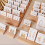 A variety of gold and silver JaxKelly Mystery Earrings are displayed on wooden stands, each pair mounted on white branded cards. This elegant, organized sale highlights unique shapes and sparkling gemstones for a surprise earring experience.
