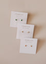 A pair of Teardrop Stud - Clear CZ earrings on a JaxKelly card, set diagonally on a neutral surface. Each stud features a clear stone in a simple 18k gold-plated setting with hypoallergenic sterling silver posts.