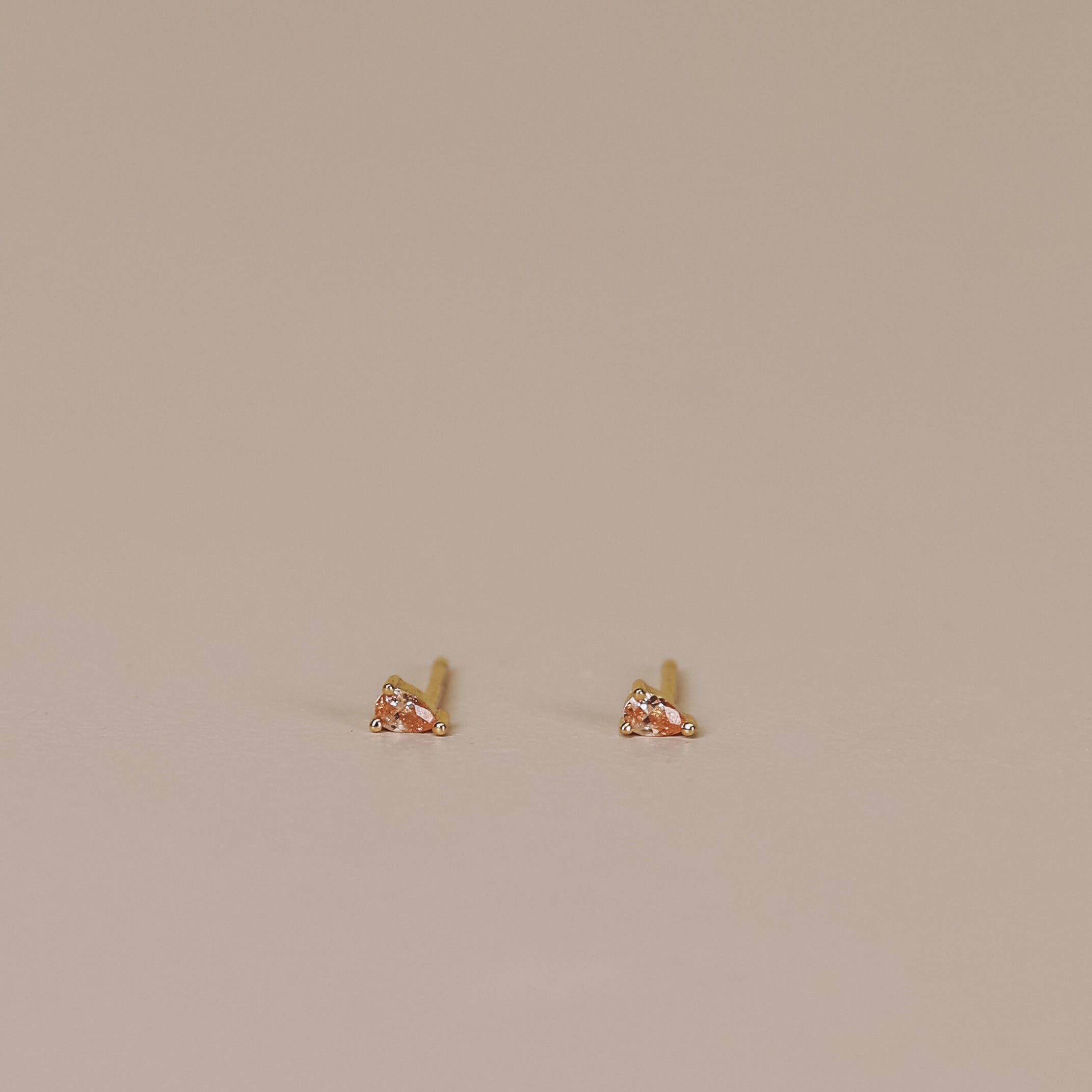Teardrop Stud - Champagne CZ: Mini teardrop earrings with 18k gold plating and sterling silver posts, minimalist design, displayed on a plain light beige surface.