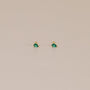 The Teardrop Stud - Emerald CZ earrings feature small 18k gold plating and sparkling green CZ stones, shown against a plain beige background.