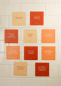 Ten waterproof Positivity Shower Affirmations™ cards in orange and red display uplifting self-affirmations in white text, arranged on a white tiled wall—perfect reusable shower cards to inspire positivity every day.