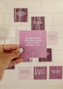 A hand with painted nails holds a wet purple Boundaries Shower Affirmations™ card in a shower. The card reads, "It's okay if others don't understand or agree with the boundaries I set." Blurry cards are visible on white tiles behind.