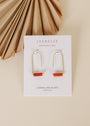 Carnelian Agate Gemstone Drop - Creativity earrings featuring rectangular orange stones on a JaxKelly card, displayed on a beige surface with a dried palm leaf in the corner.