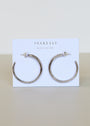 A pair of Silver Everyday Hoop - Large sterling silver earrings are shown on a white JaxKelly card with "Wear Good Vibes" printed, set against a neutral, minimalistic background.