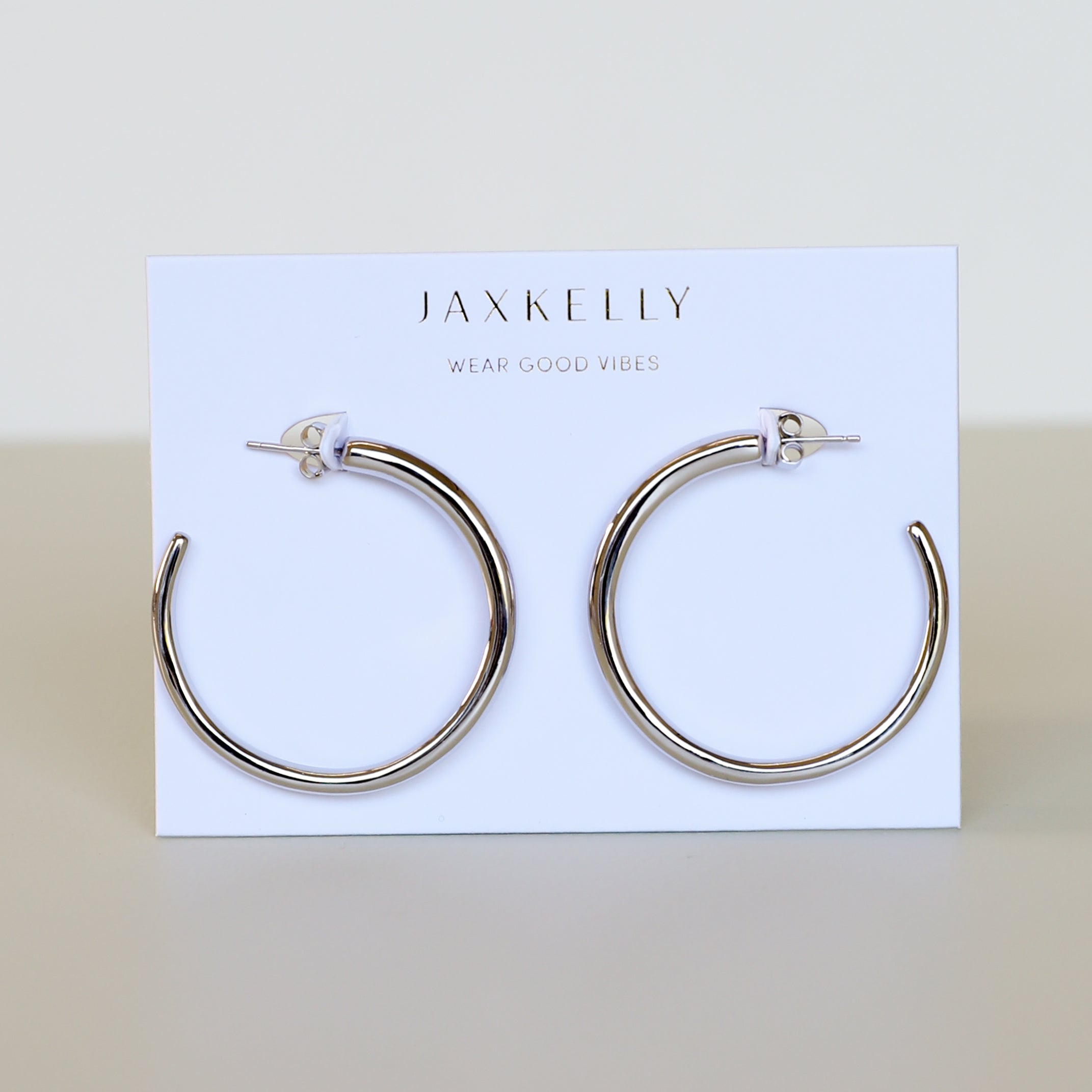 A pair of Silver Everyday Hoop - Large sterling silver earrings are shown on a white JaxKelly card with "Wear Good Vibes" printed, set against a neutral, minimalistic background.