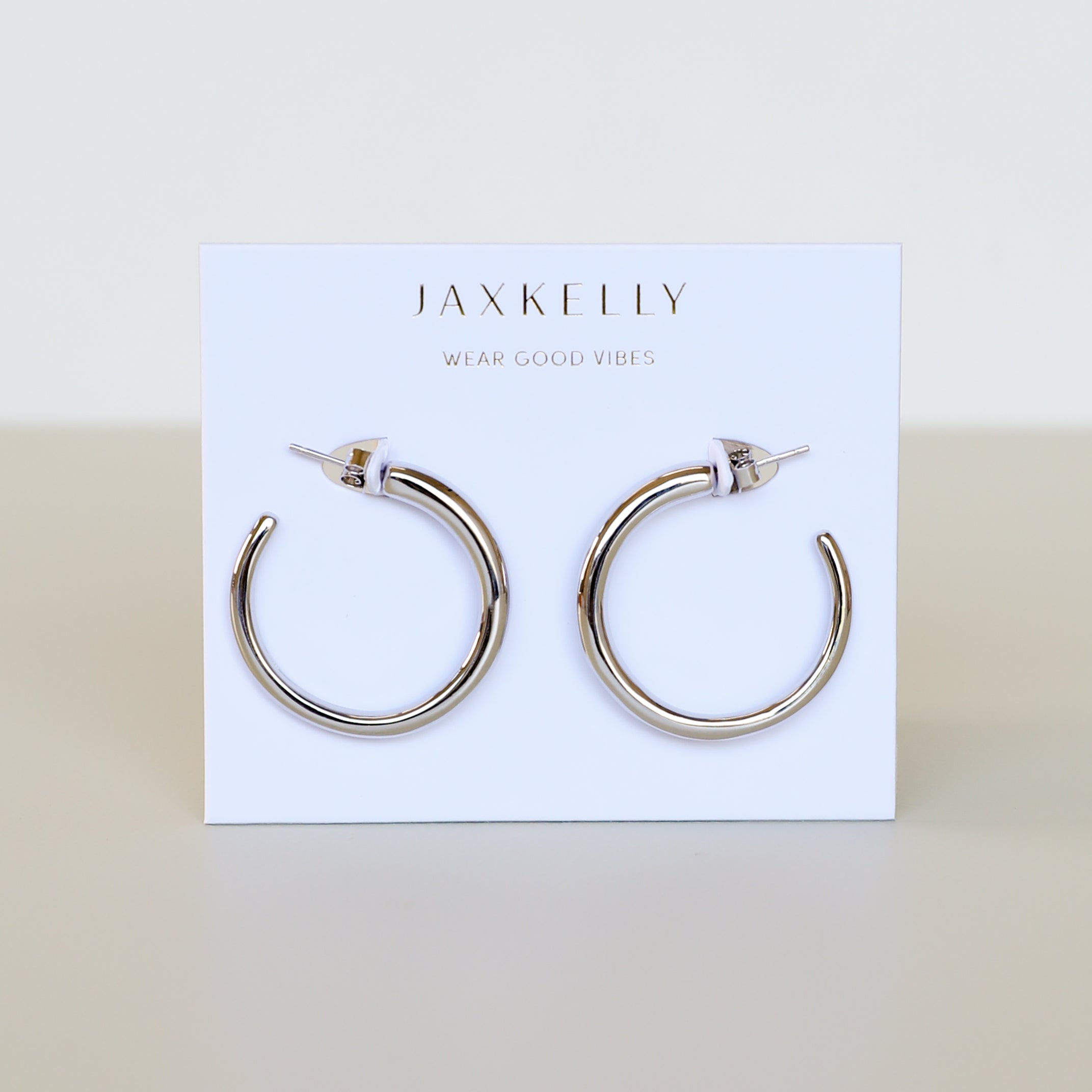 The Silver Everyday Hoop - Medium, crafted from sterling silver, is displayed on a white card featuring the JaxKelly logo and "Wear Good Vibes" in gold, making it an ideal choice for fans of classic jewelry.