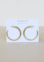 The Gold Everyday Hoop - Large, 18k gold plated bold hoops, are displayed on a white card with JaxKelly and Wear Good Vibes printed on it against a neutral background.