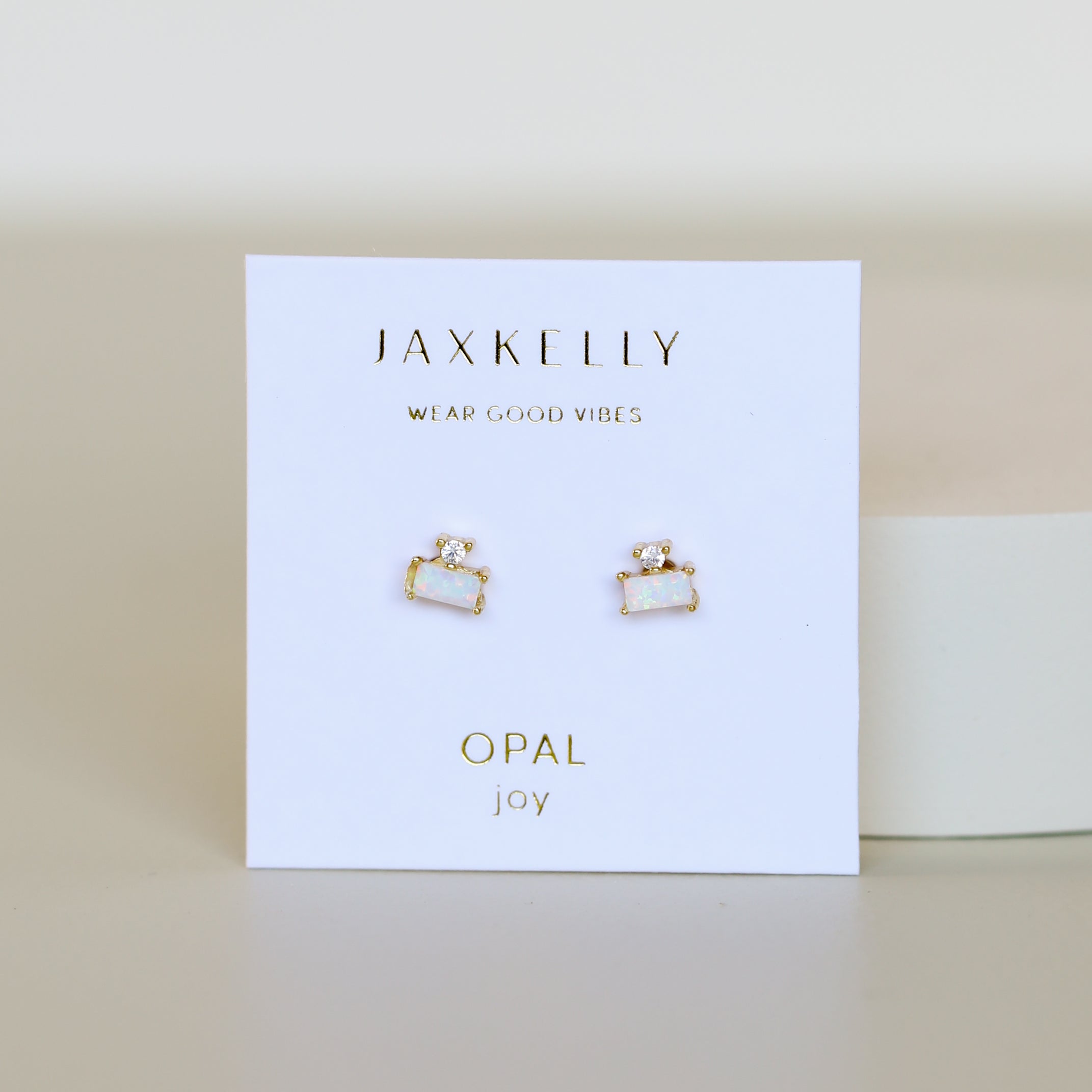 The White Opal Double Stud Stack features gold-framed white opal studs with 18k gold plating, displayed on a white JaxKelly card printed in gold with "Wear Good Vibes," "OPAL," and "joy.