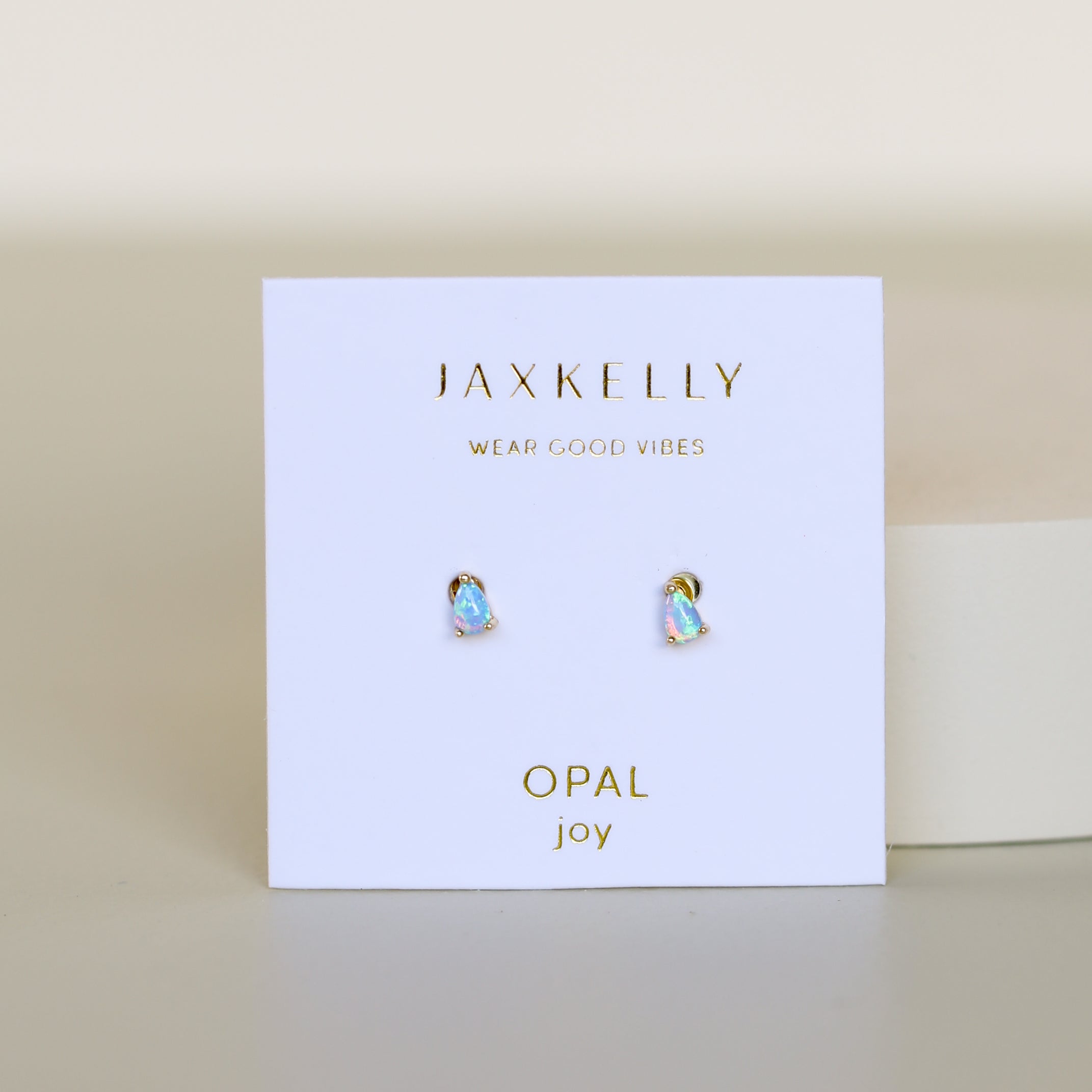 A pair of Teardrop Stud - Fire Opal earrings shown on a white card with gold "JAXKELLY Wear Good Vibes" and "OPAL joy" text, set against a light, neutral background.