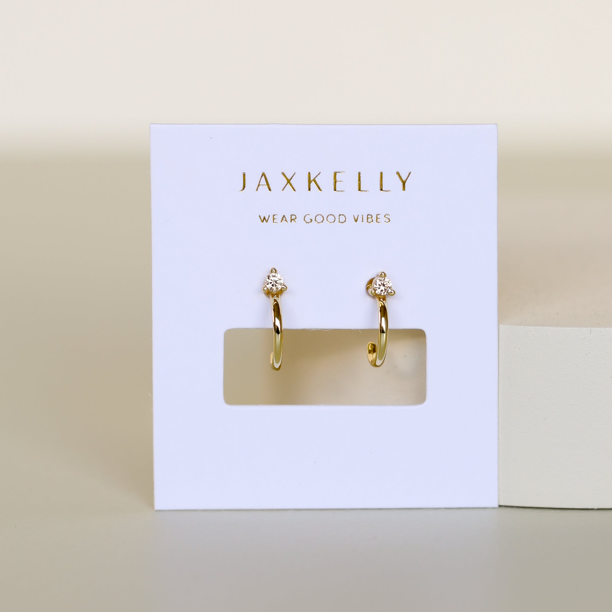 The Open Mini Hoop Earring - Champagne features 18K gold plating and sparkling champagne CZ stones, displayed on a white JaxKelly card with "Wear Good Vibes" against a neutral, minimalist background.