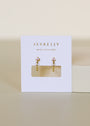 The Open Mini Hoop Earring - Pink features gold hoops adorned with small pink CZ stones, displayed on a white JaxKelly card reading "WEAR GOOD VIBES" in gold lettering. The neutral background enhances its minimalistic look.