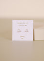 A pair of White Opal Mini Energy Gems - Joy studs, heart-shaped with 18k gold plating, displayed on a white “JAX KELLY, WEAR GOOD VIBES, OPAL, joy” card against a light beige background.