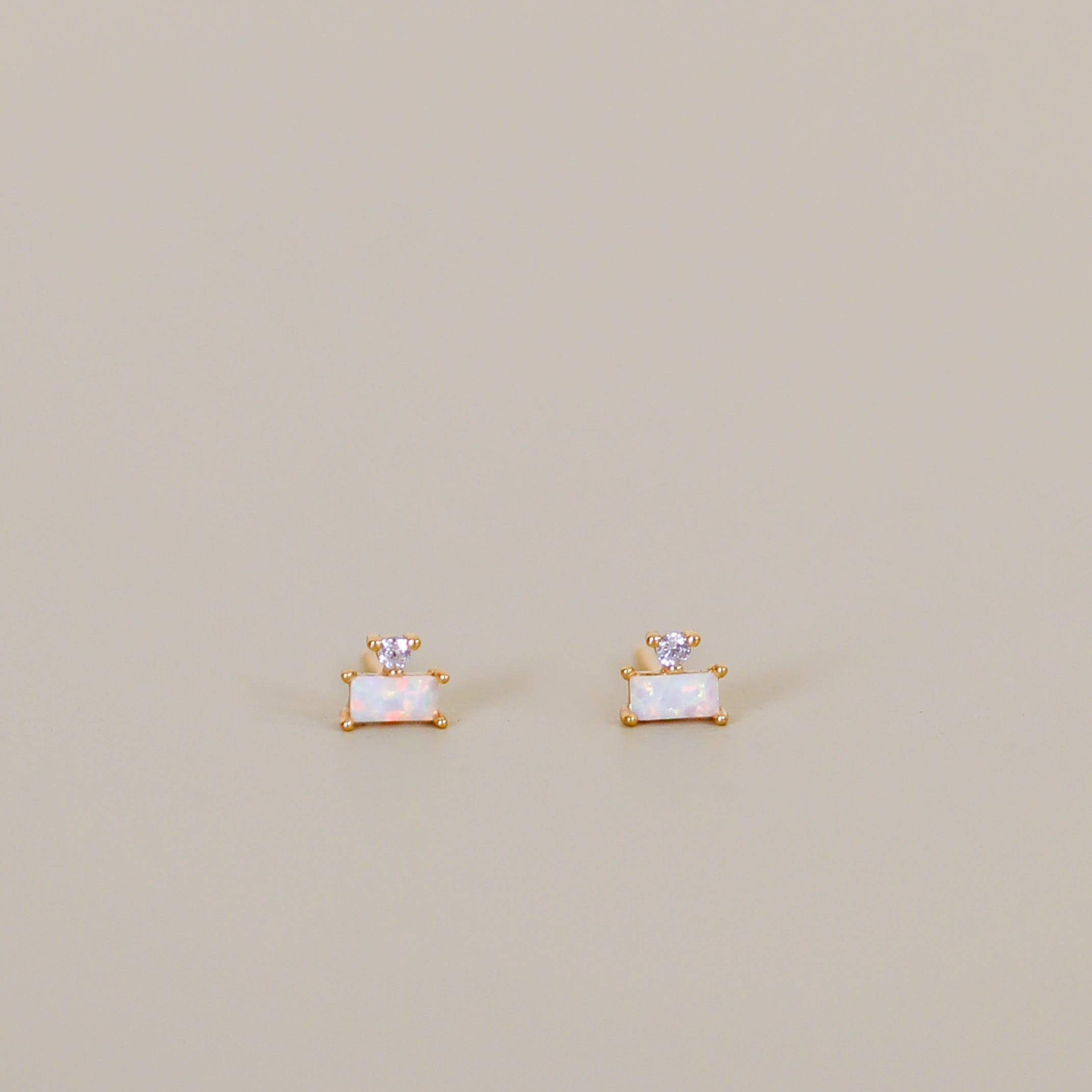 The White Opal Double Stud Stack features small rectangular white opal stones set in 18k gold plating, each accented with a tiny round lab-grown clear gemstone, displayed on a simple light beige background.