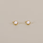 The Simple Stud - White Opal features small, round lab-grown white opal earrings set in minimalist 18k gold plated bezels, shown against a plain beige background.