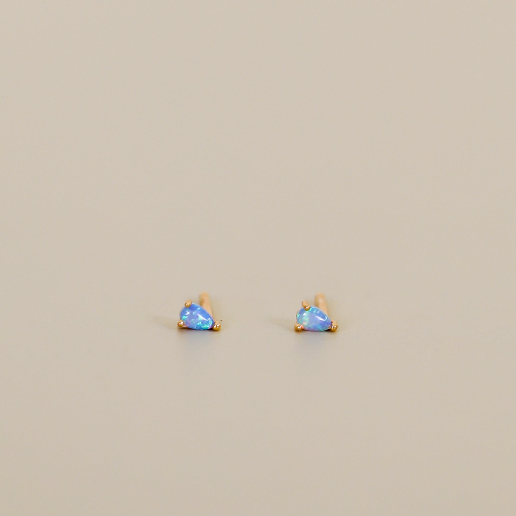 The Teardrop Stud - Fire Opal earrings feature lab-grown fire opal gemstones set in gold, shown on a plain light beige background.