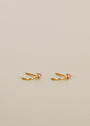 The Open Mini Hoop Earring - Pink features a tiny pink CZ stone on each small hoop, shown against a plain light beige background.