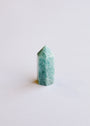 The Mini Amazonite Quartz Crystal Point stands upright on a white surface, displaying its polished finish and soothing blue-green hue, perfect for adding a calming touch to any space.