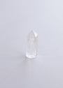 The Mini Clear Quartz Crystal Point, featuring small inclusions, stands upright on a light-colored surface against a soft, minimal background.