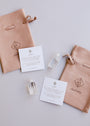 A peach-colored suede pouch labeled "JaxKelly" sits beside a Mini Clear Quartz Crystal Point and an info card explaining the gemstone’s meaning, all arranged on a light background.