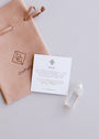 The Mini Clear Quartz Crystal Point, an informational card about clear quartz, and a suede pouch labeled JaxKelly are arranged on a light surface.