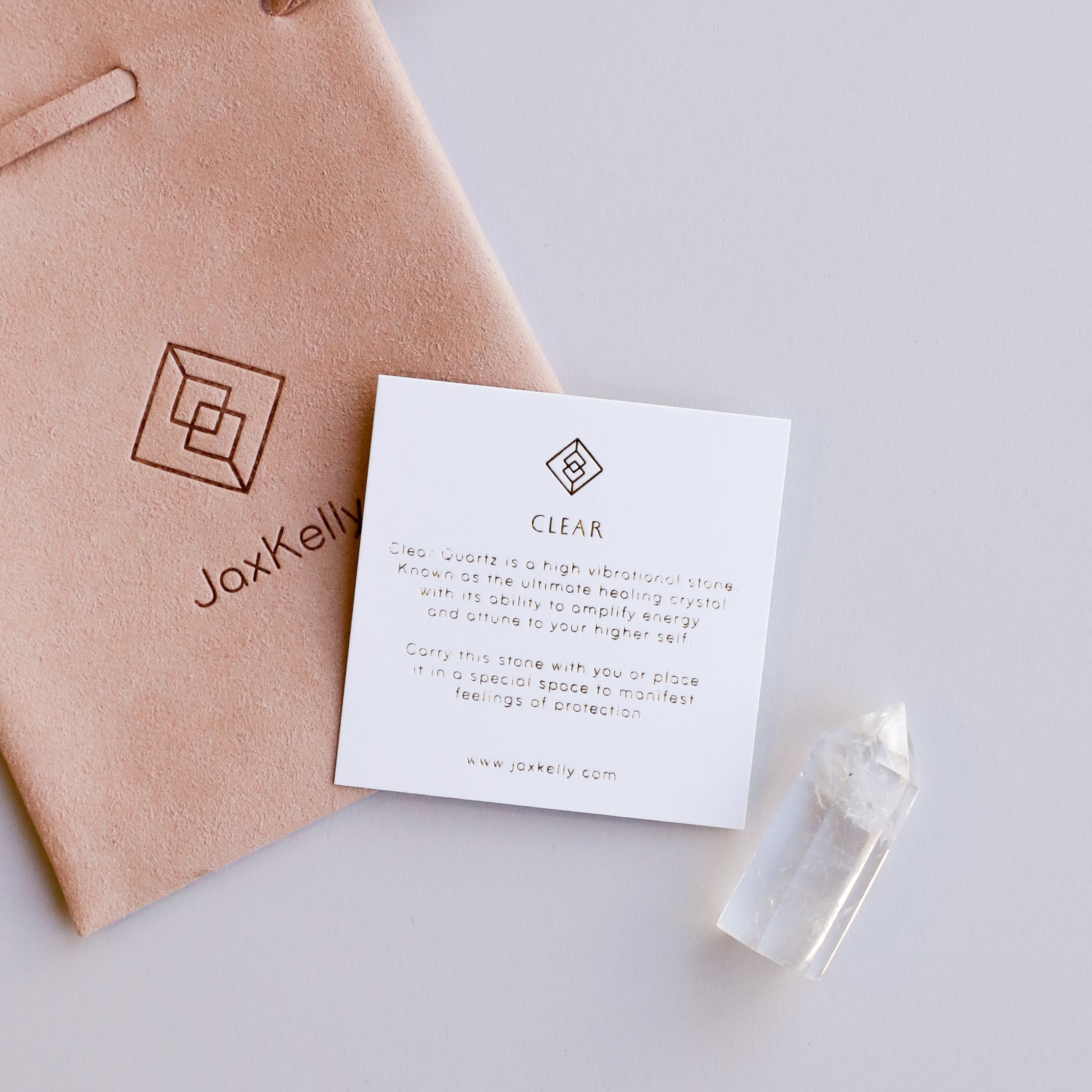The Mini Clear Quartz Crystal Point, an informational card about clear quartz, and a suede pouch labeled JaxKelly are arranged on a light surface.