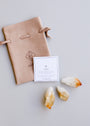 The Raw Citrine Crystal Set includes a beige suede drawstring pouch, an informational card about citrine, and three raw Citrine stones, all displayed on a light gray surface.