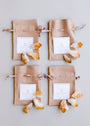 Four beige drawstring pouches with white labels are arranged in a grid on a light background, surrounded and topped with Raw Citrine Crystal Set stones and crystal gems.