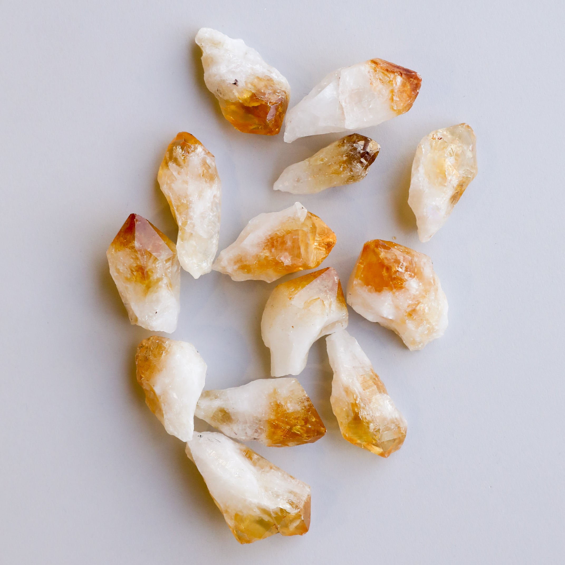 The Raw Citrine Crystal Set features several small, rough stones in white and golden-yellow hues, arranged in a scattered pattern on a light gray background.