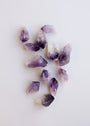 The Raw Amethyst Crystal Set features several purple and white stones, known for enhancing intuition, scattered on a plain white background.